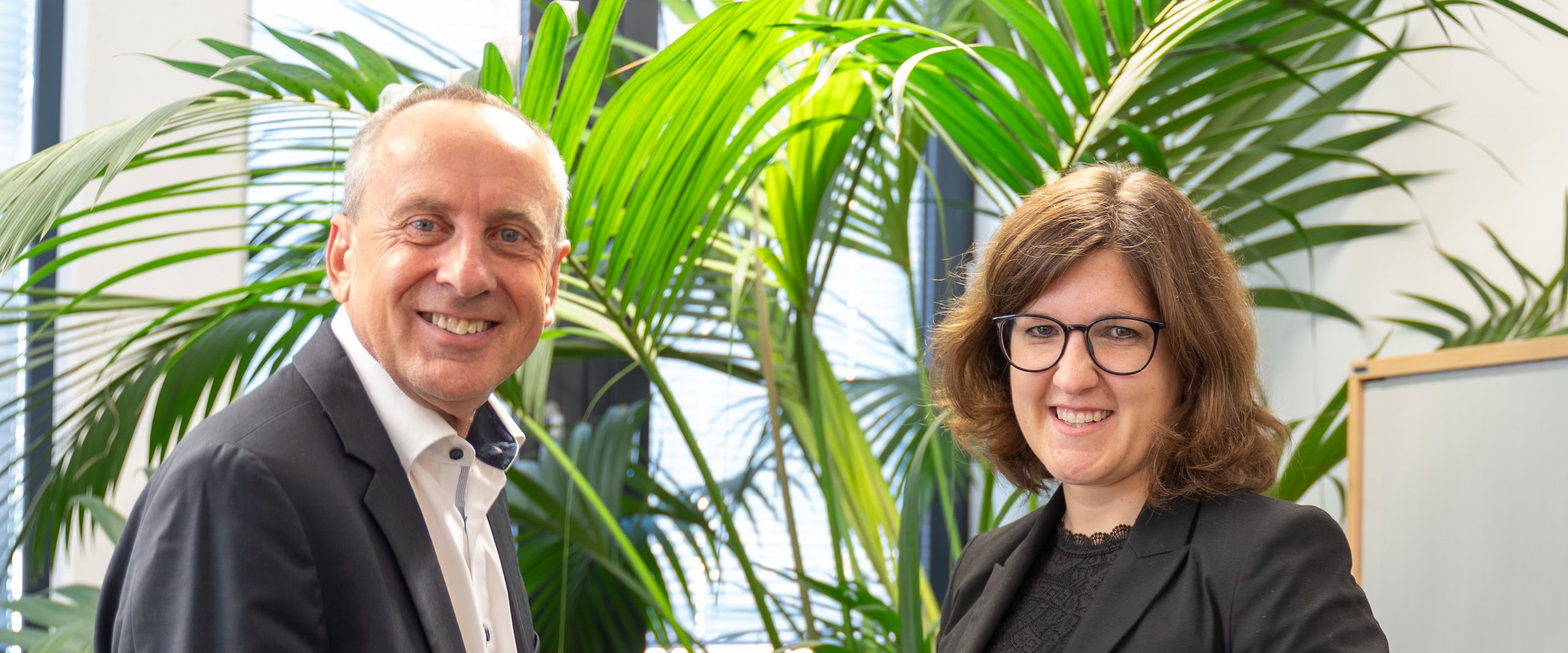 Mann und Frau halten gemeinsam eine Urkunde und lachen in die Kamera