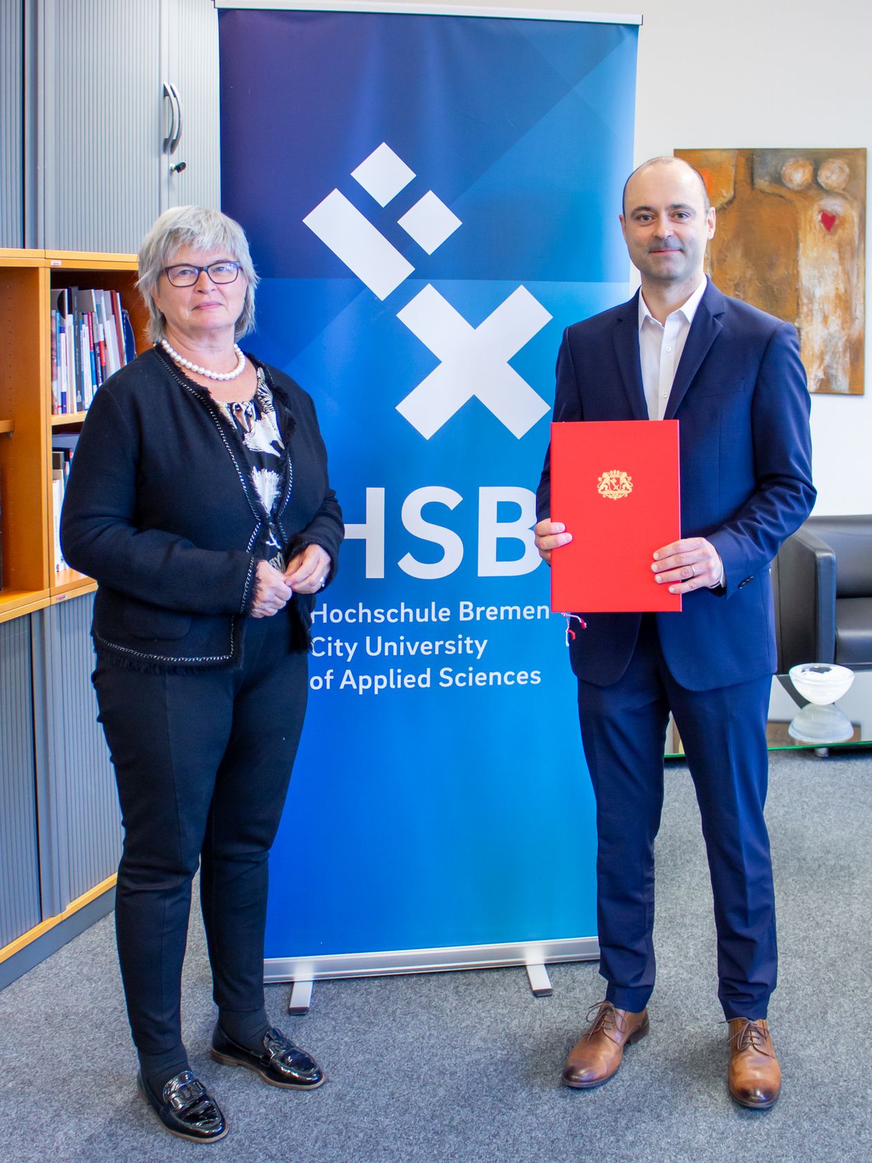 Frau und Mann stehen vor Banner. der Mann hält eine Urkunde.