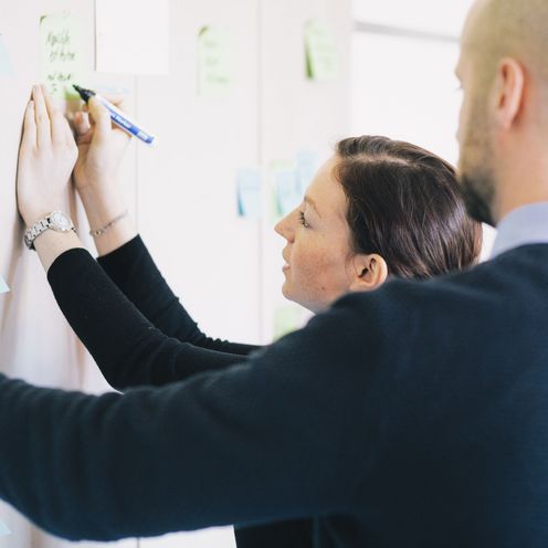 Zwei HSB Studierende stehen vor einer Pinnwand mit vielen Zetteln und h&auml;ngen weitere Zettel dazu.