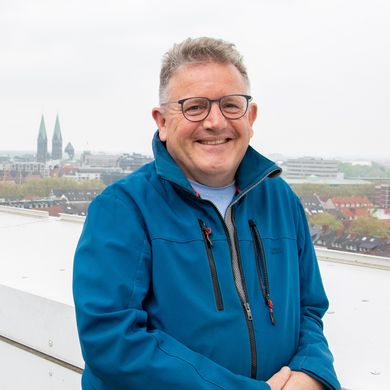 Mann steht am Geländer und lacht in die Kamera