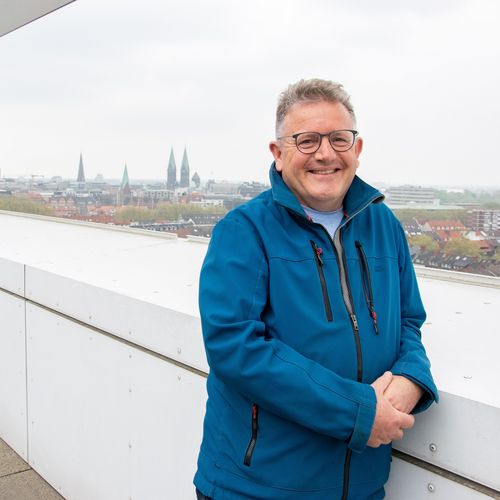 Mann steht am Geländer und lacht in die Kamera