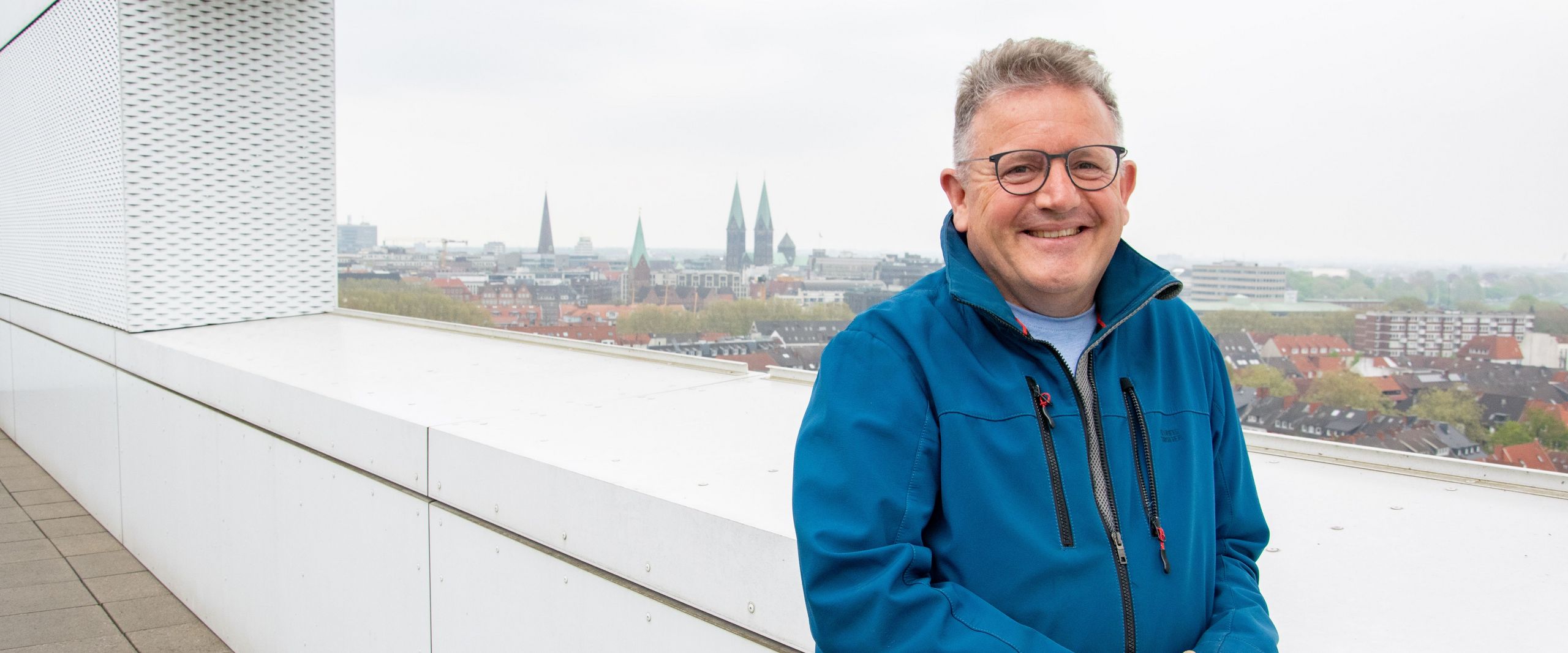 Mann steht am Geländer und lacht in die Kamera