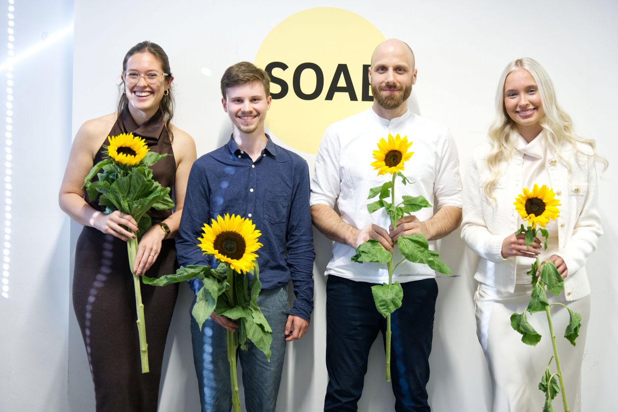 Die vier Preisträger:innen der Sommerschau 2026 präsentieren sich gemeinsam mit Sonnenblumen vor dem Logo der School of Architecture Bremen. Die Ausgezeichneten strahlen in die Kamera und feiern ihre besonderen Leistungen.