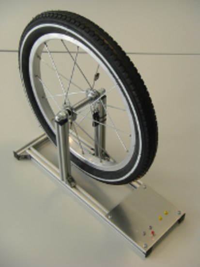 Fahrradmodell mit Tachosensor Auf dem Bild ist ein Fahrradreifen in einer Halterung zu erkennen. Die Halterung sorgt dafür, dass der Reifen sich bewegen kann. Die Halterung ist silber.