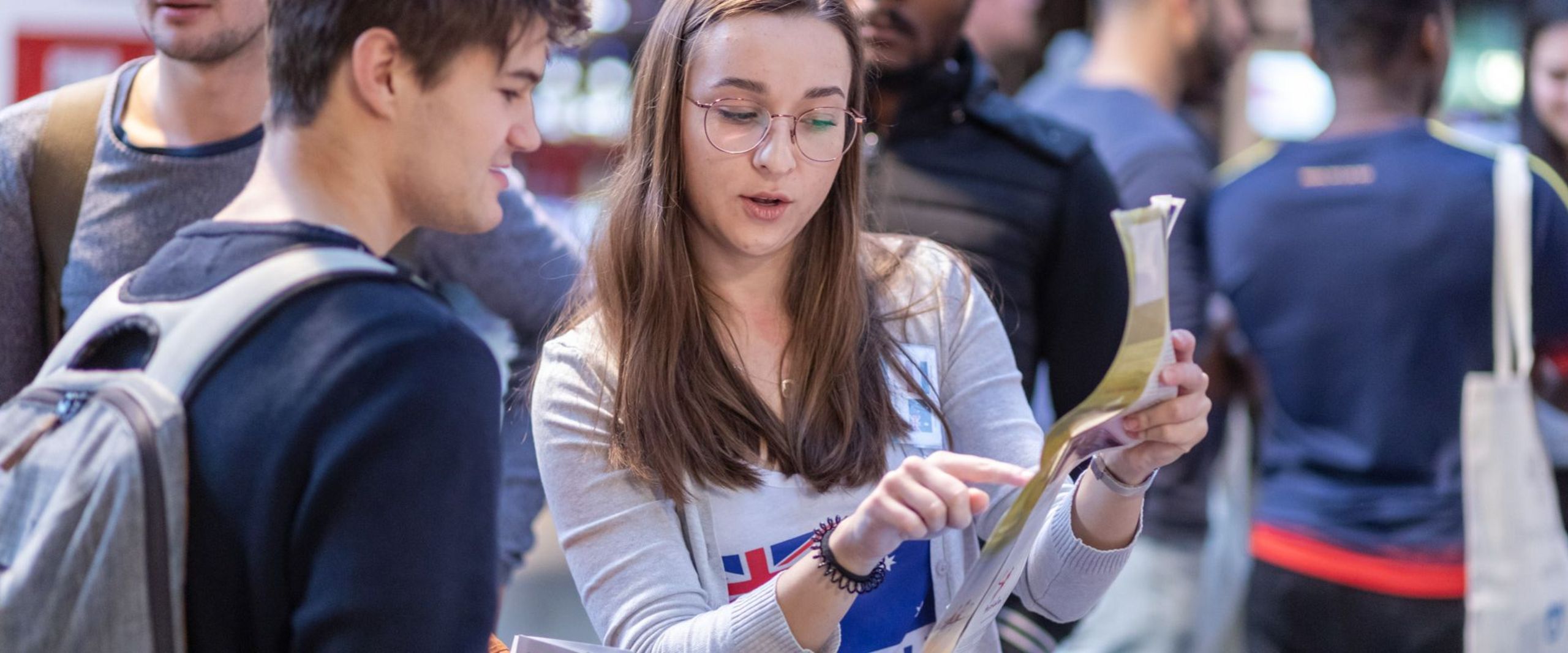 Studierende sind auf einer Messe und zwei unterhalten sich im Vordergrund.