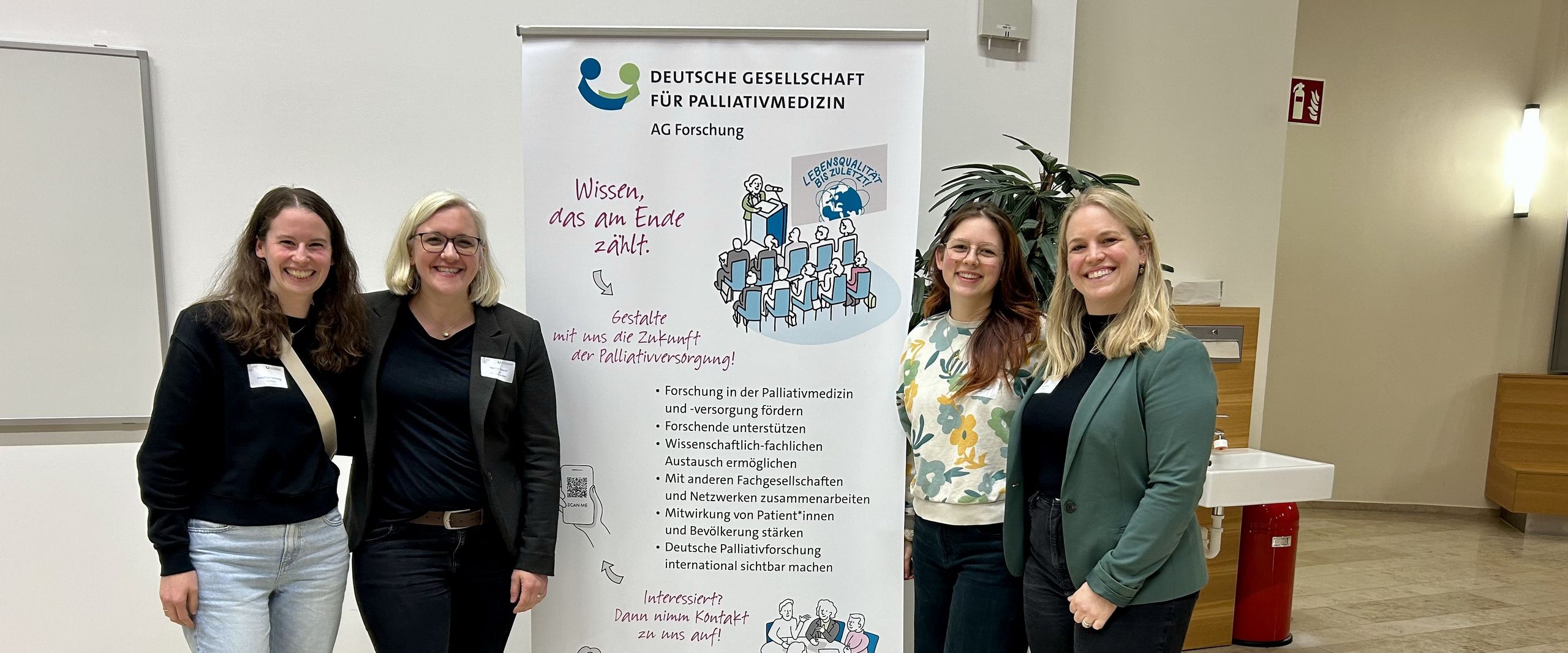 Gruppenbild mit vier Frauen. In der Mitte ein Roll-up