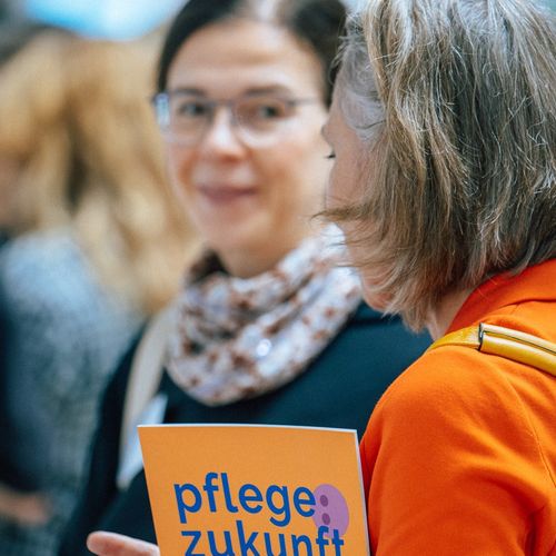 Zwei Teilnehmerinnen reden miteinander. Eine trägt die Broschüre Pflegezukunft auf dem Arm.