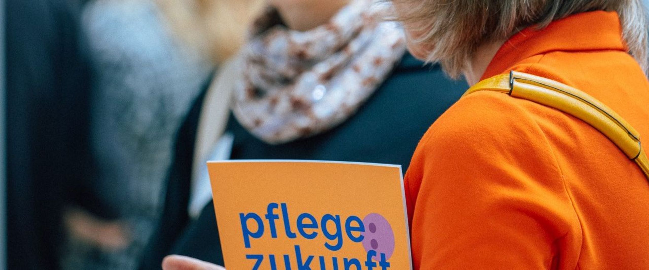 Zwei Teilnehmerinnen reden miteinander. Eine trägt die Broschüre Pflegezukunft auf dem Arm.