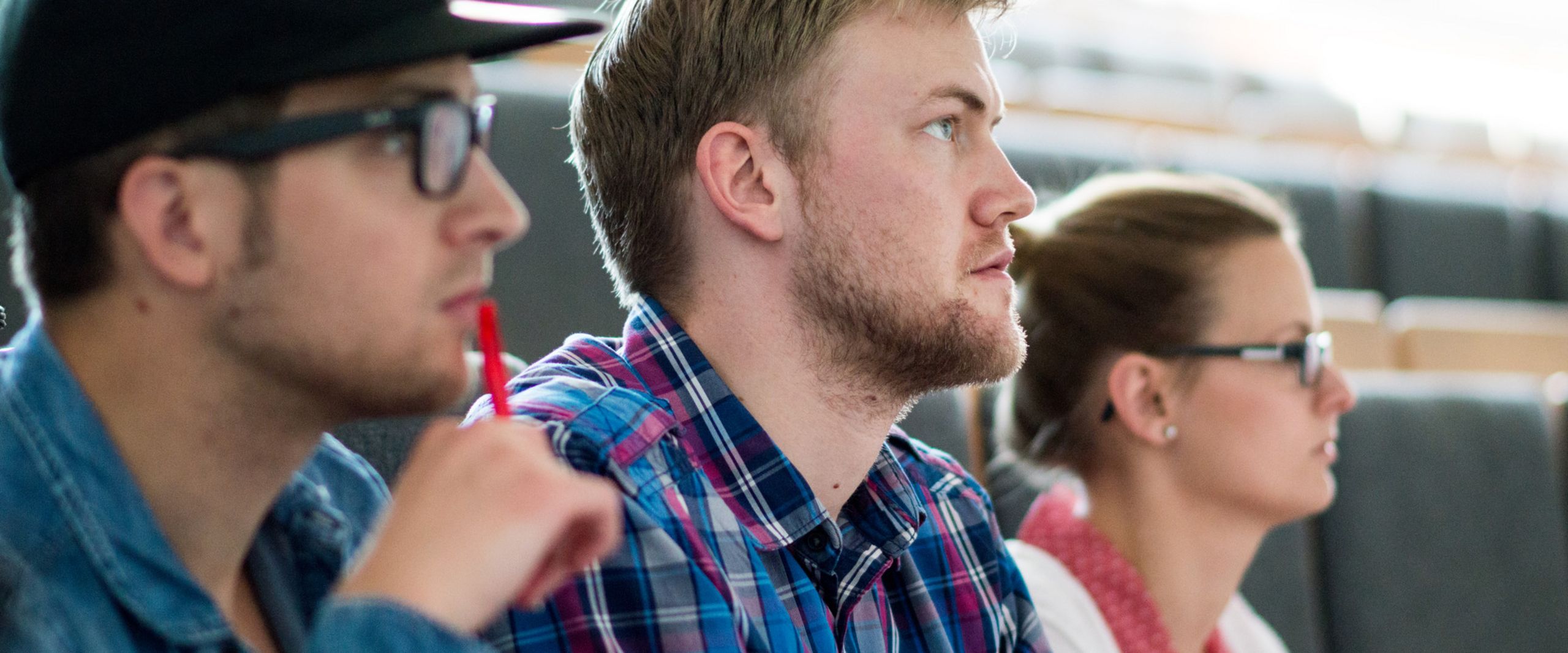 Studierende im Hörsaal Drei Studierende sitzen im Hörsaal und gucken konzentriert nach vorne.
