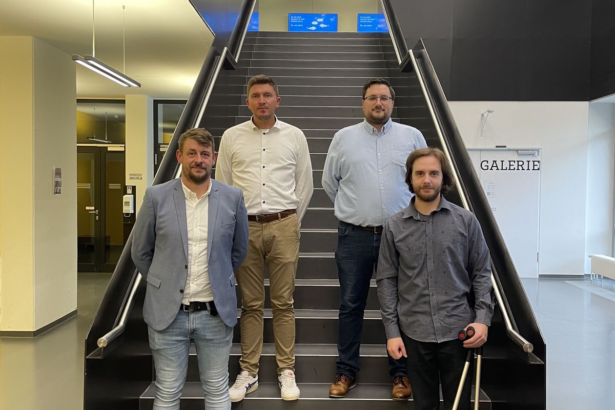 Vier Männer stehen an einer Treppe und lächeln in die Kamera.