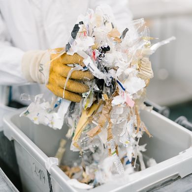Person in Kittel und Handschuhen hält geschredderten Müll.