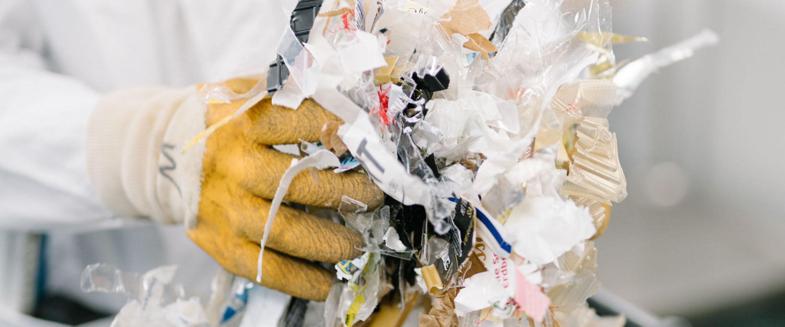Person in Kittel und Handschuhen hält geschredderten Müll.