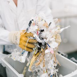 Person in Kittel und Handschuhen hält geschredderten Müll.