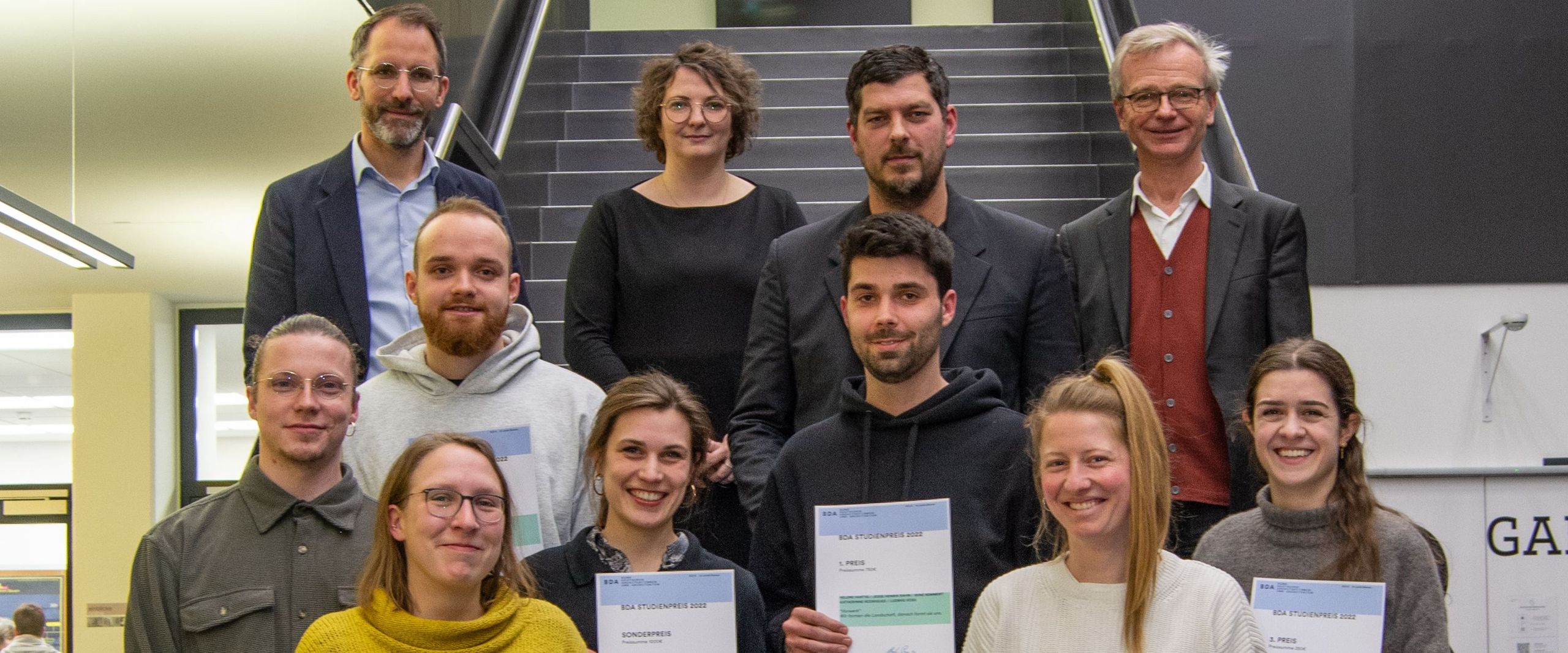 Gruppenbild mit Männern und Frauen auf einer Treppe. Einige halten Urkunden