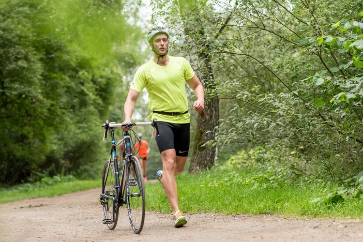 Training TriRunners Ein Sportler läuft durch einen Wald und schiebt dabei ein Rennrad.