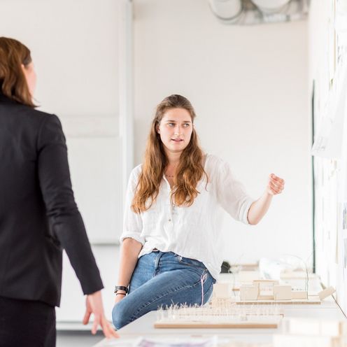 Eine Studentin pr&auml;sentiert Prof. Andrea Dung und einem Kommilitonen ihre architektonischen Entw&uuml;rfe.