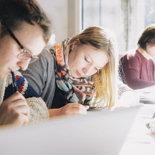 3 Personen sitzen nebeneinander und schreiben konzentriert