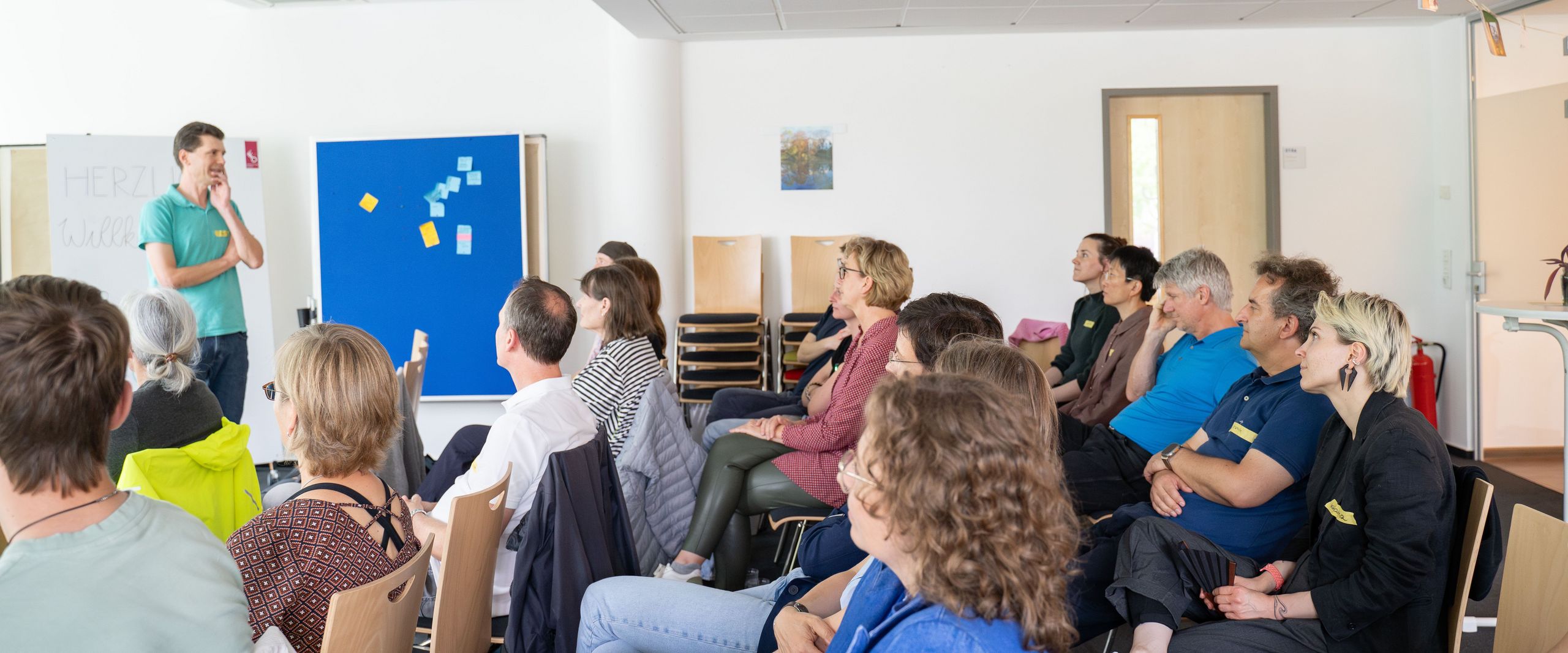 Auf dem Bild ist ein Vortragender zusehen, der mit dem Publikum interagiert. 