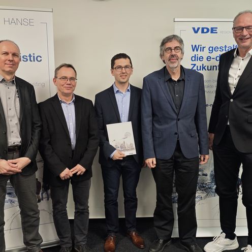 Gruppenbild mit M&auml;nnern im Anzug, die vor Roll-ups stehen. Einer in der Mitte h&auml;lt eine Urkunde.