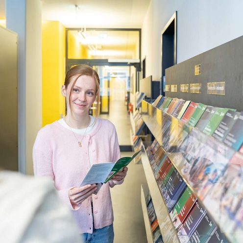 Auf dem Bild ist eine junge Frau zusehen. Sie h&auml;lt einen Flyer in der Hand und schaut knapp an der Kamera vorbei. 