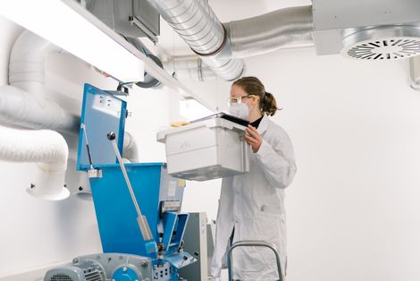 Kreislaufwirtschaft Studentin steht auf einer Leiter und hebt einen weißen Kasten.