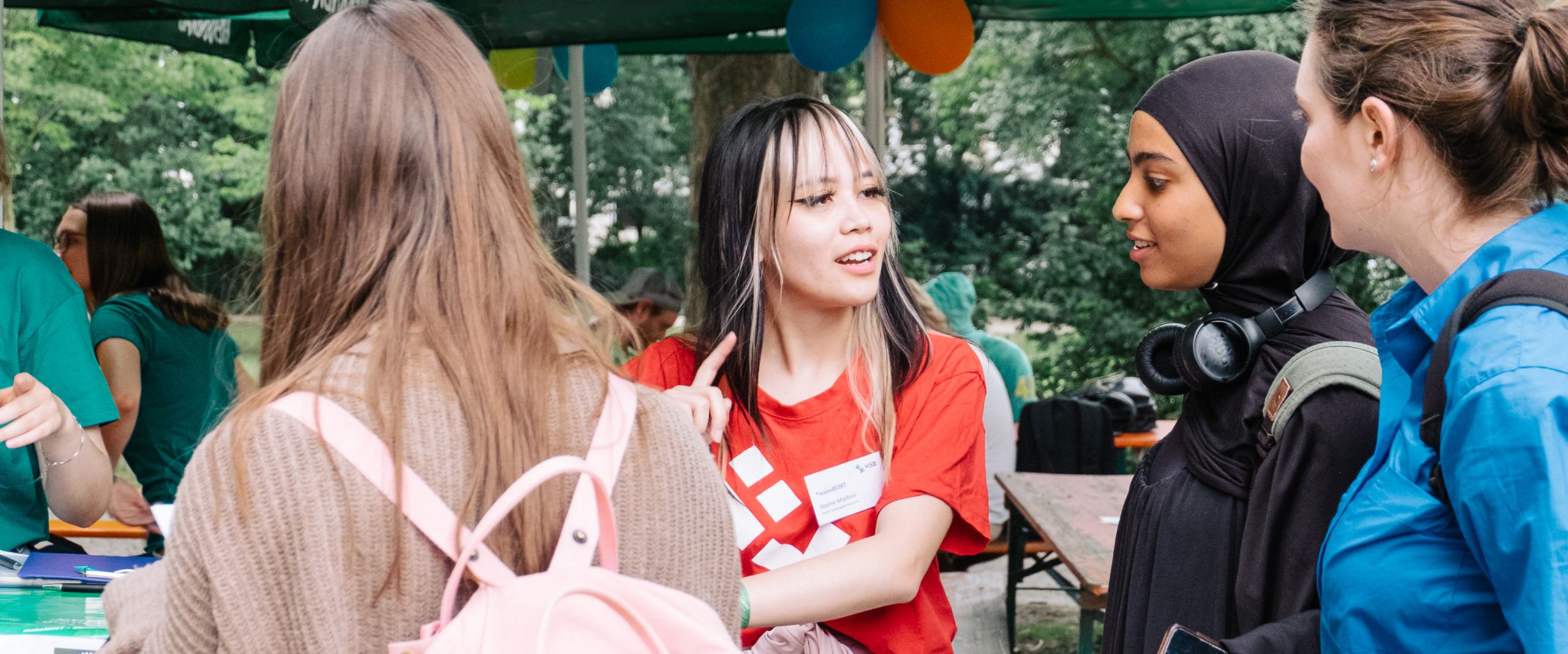 Anmeldung und Support beim meetMINT-Sommerfest 2023 3 Studentinnen melden sich bei einer Hilfskraft für das Sommerfest an.