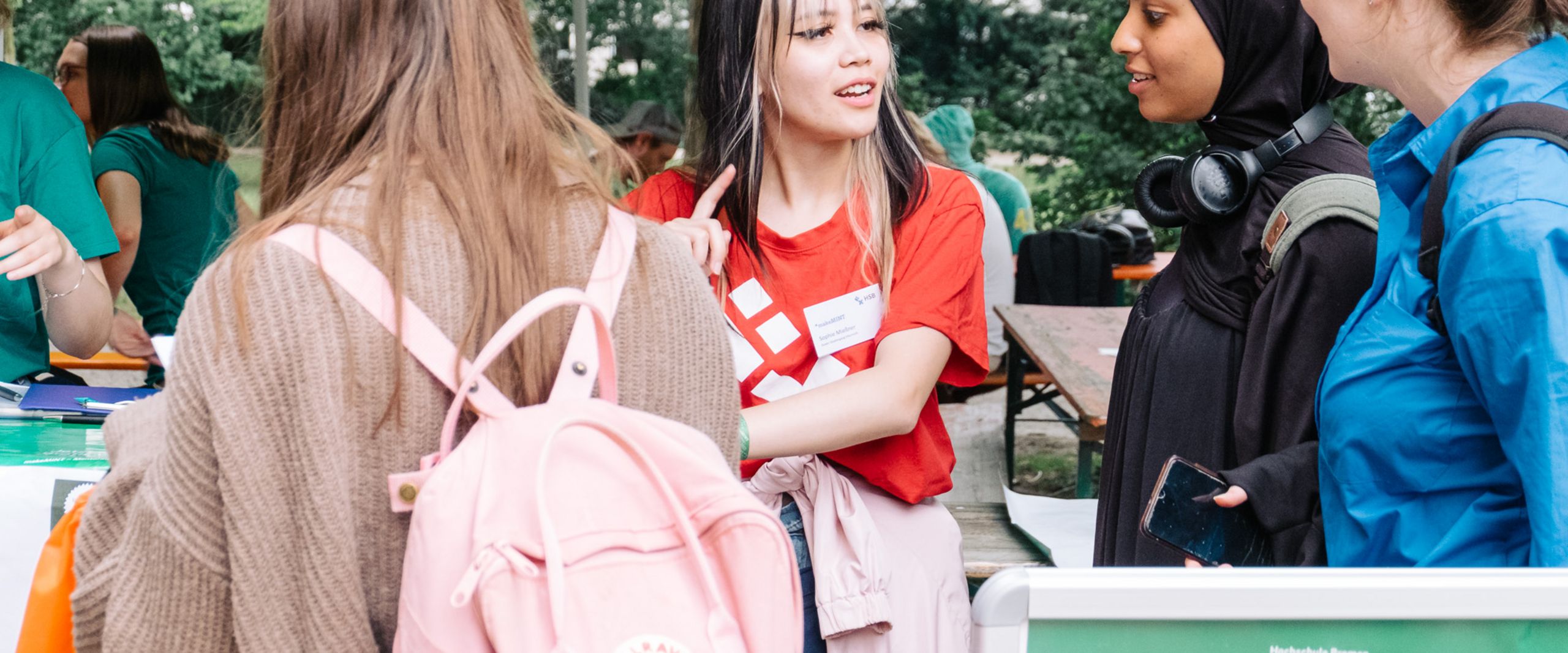 3 Studentinnen melden sich bei einer Hilfskraft f&uuml;r das Sommerfest an. 