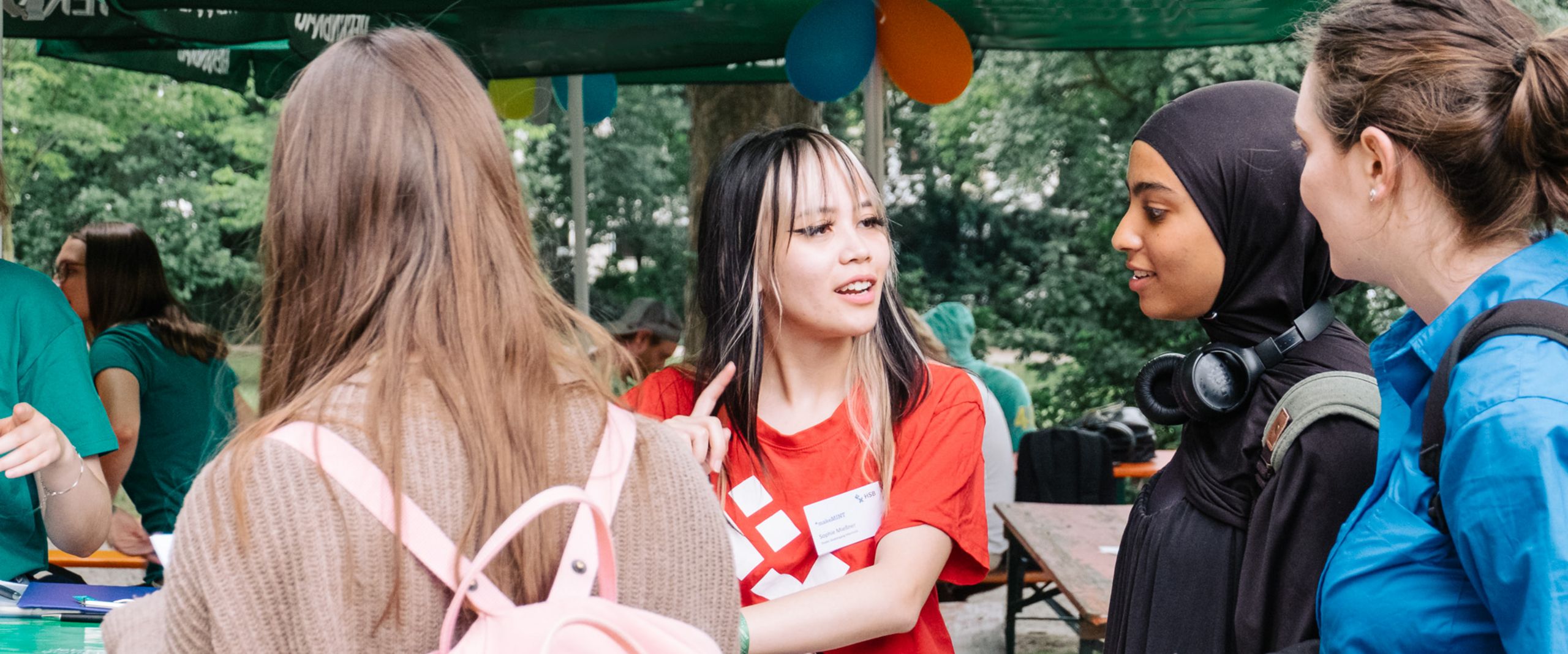 Anmeldung und Support beim meetMINT-Sommerfest 2023 3 Studentinnen melden sich bei einer Hilfskraft für das Sommerfest an.