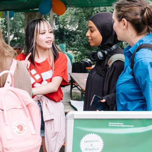 3 Studentinnen melden sich bei einer Hilfskraft f&uuml;r das Sommerfest an. 