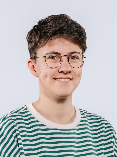 Auf dem Bild ist Saskia Dohmen zusehen. Sie hat kurzes dunkelbraunes Haar und trägt eine runde Brille. Ihr T-Shirt ist grün-weiß gestreift. 