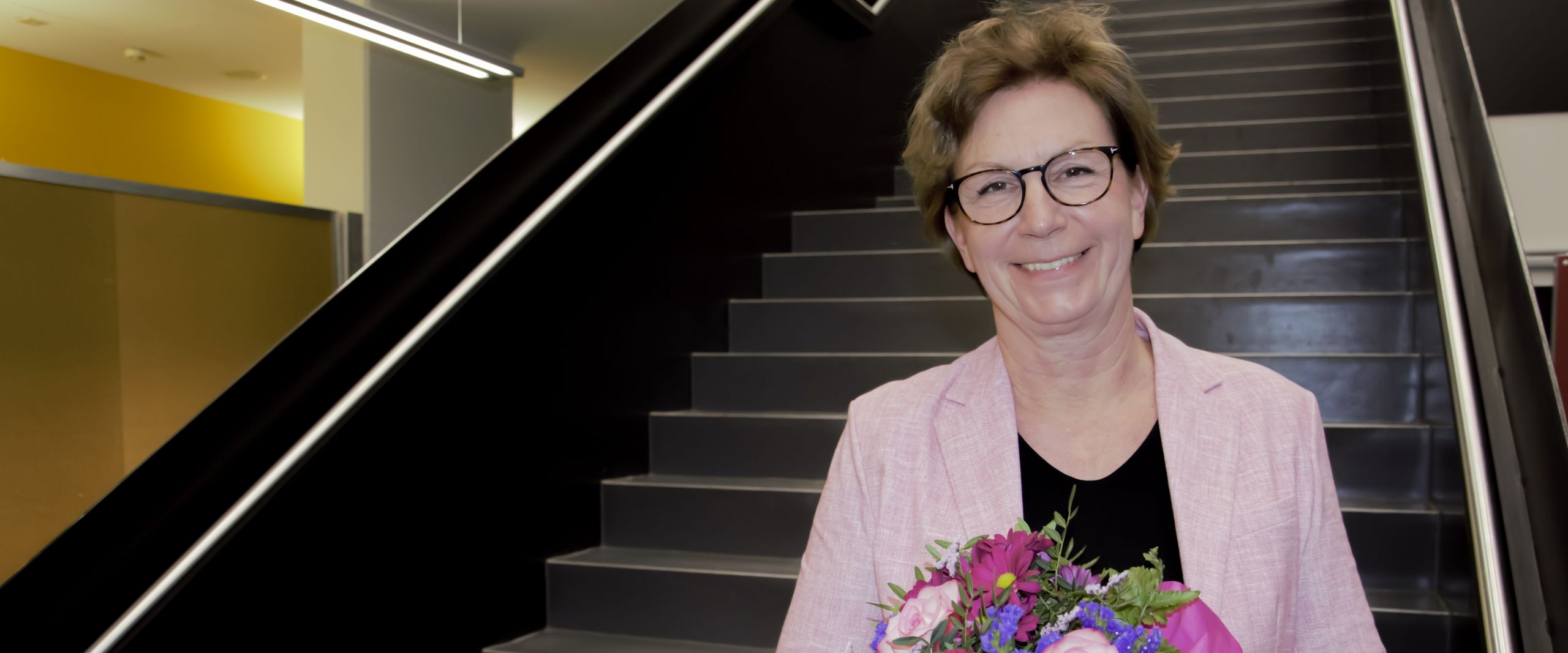 Frau mit Blumenstrauß steht auf Treppe und lacht in die Kamera