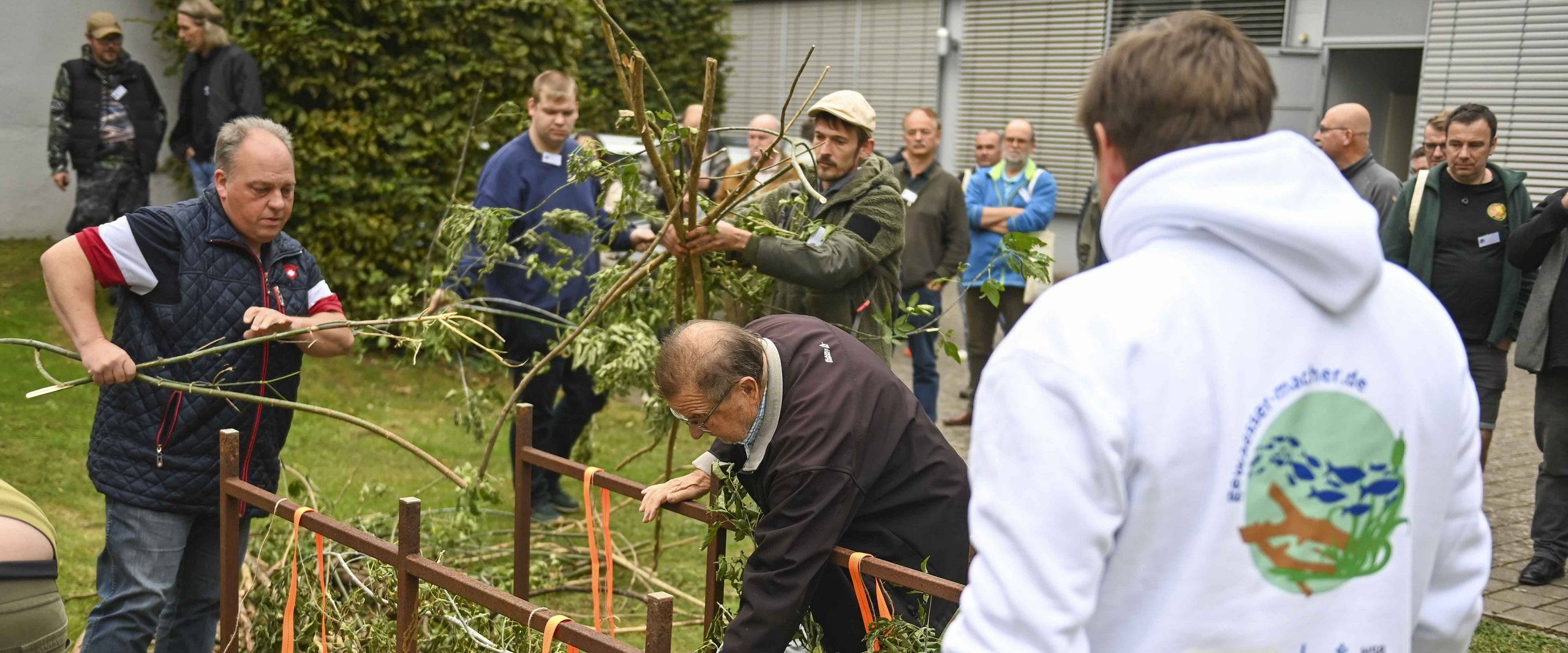 M&auml;nner stehen im Freien vor Holzkonstrukten