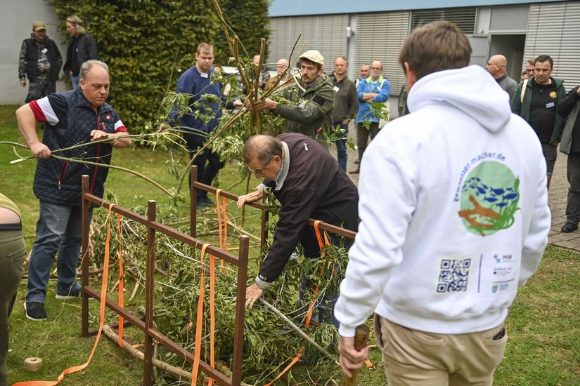 M&auml;nner stehen im Freien vor Holzkonstrukten