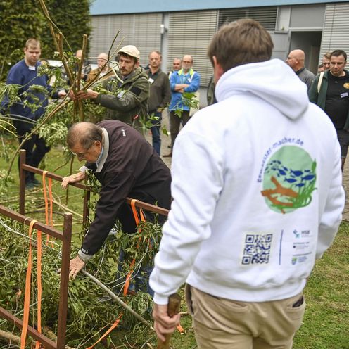 M&auml;nner stehen im Freien vor Holzkonstrukten