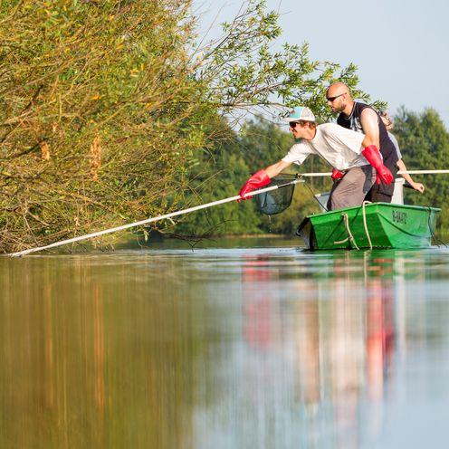 Zwei M&auml;nner im Boot auf einem See arbeiten an einer Uferb&ouml;schung.