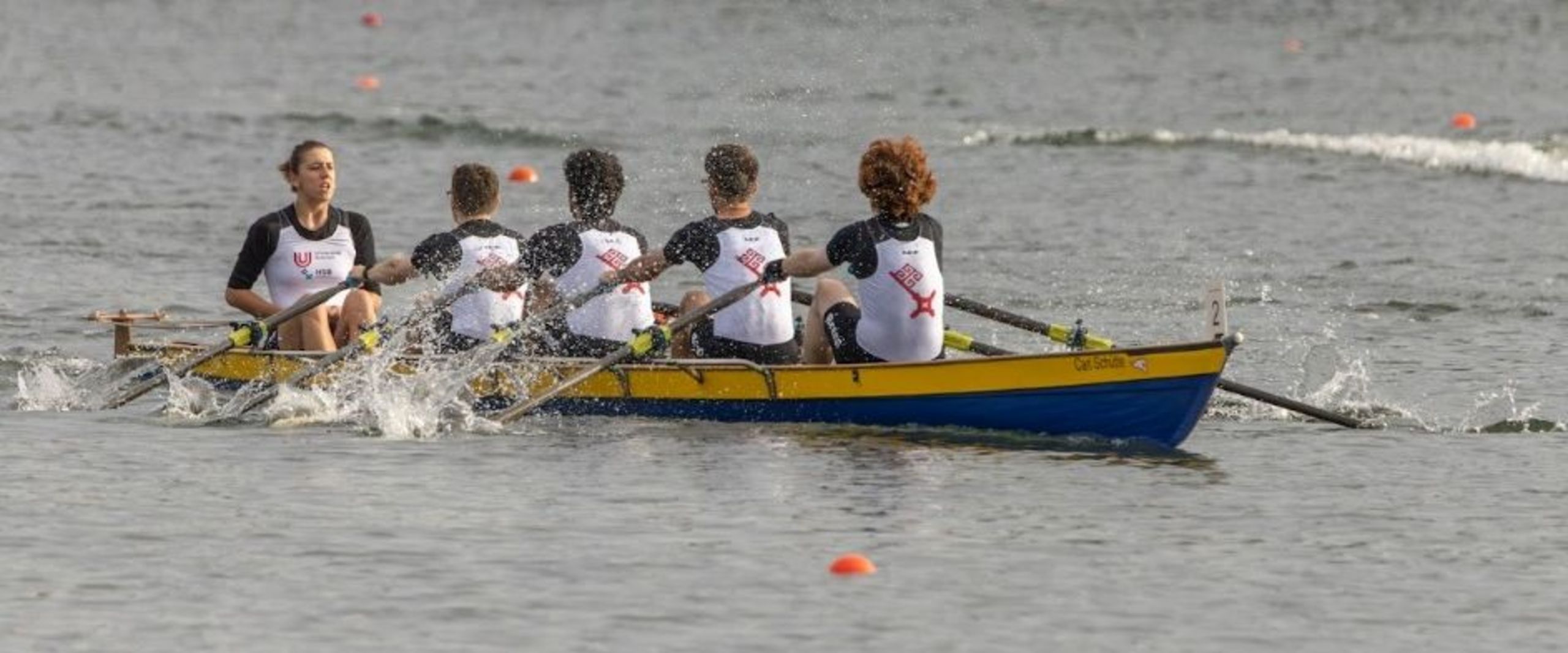 Vier Ruderer sitzen gemeinsam während der Deutschen Hochschulmeisterschaft Rudern in einem Boot. Vor ihnen sitzt eine Steuerfrau
