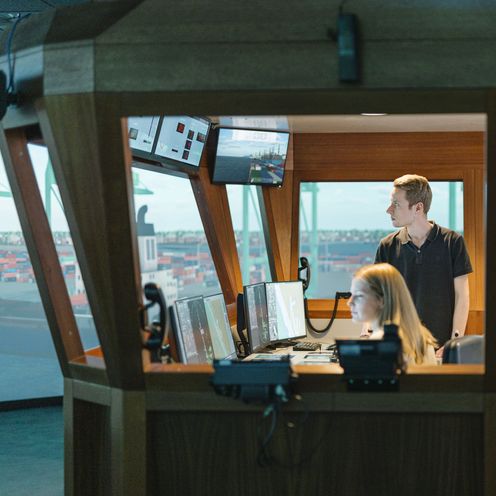 Junge M&auml;nner und eine Frau sitzen und arbeiten in einem Schiffssimulator.