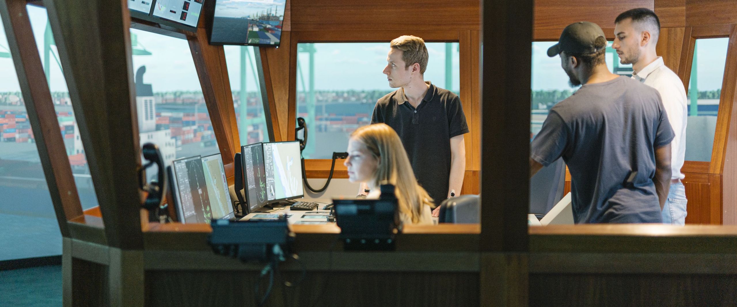 Junge Männer und eine Frau sitzen und arbeiten in einem Schiffssimulator.