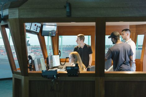 Junge Männer und eine Frau sitzen und arbeiten in einem Schiffssimulator.