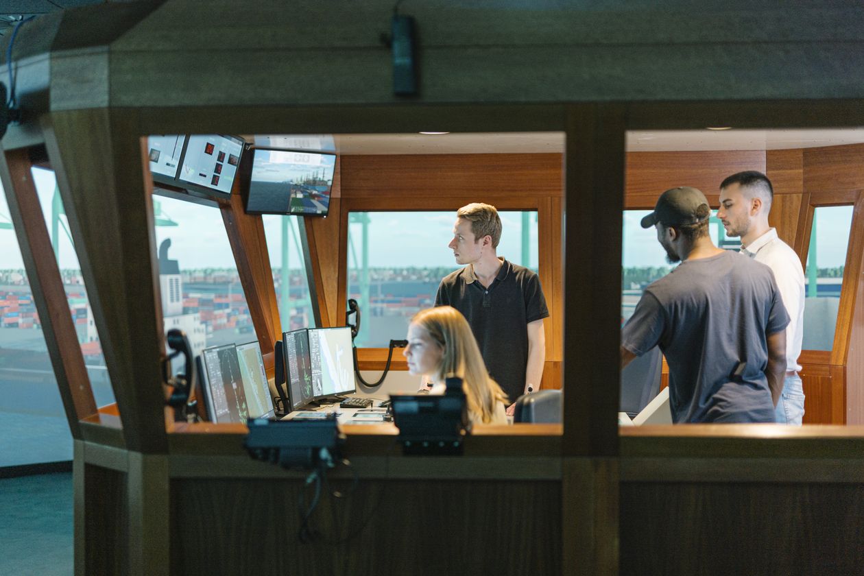 Junge Männer und eine Frau sitzen und arbeiten in einem Schiffssimulator.