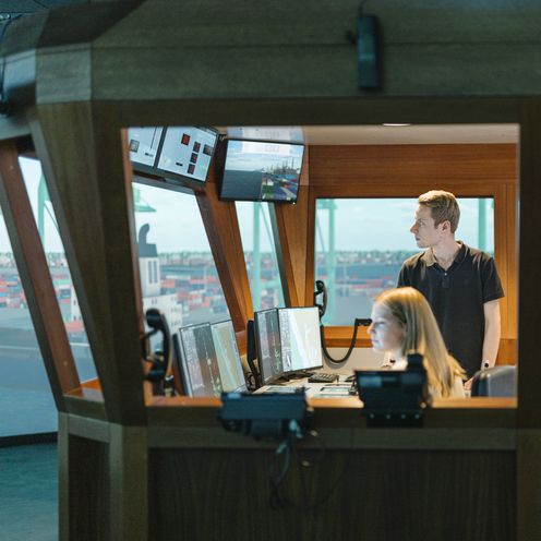 Junge M&auml;nner und eine Frau sitzen und arbeiten in einem Schiffssimulator.