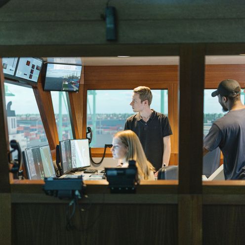 Junge M&auml;nner und eine Frau sitzen und arbeiten in einem Schiffssimulator.
