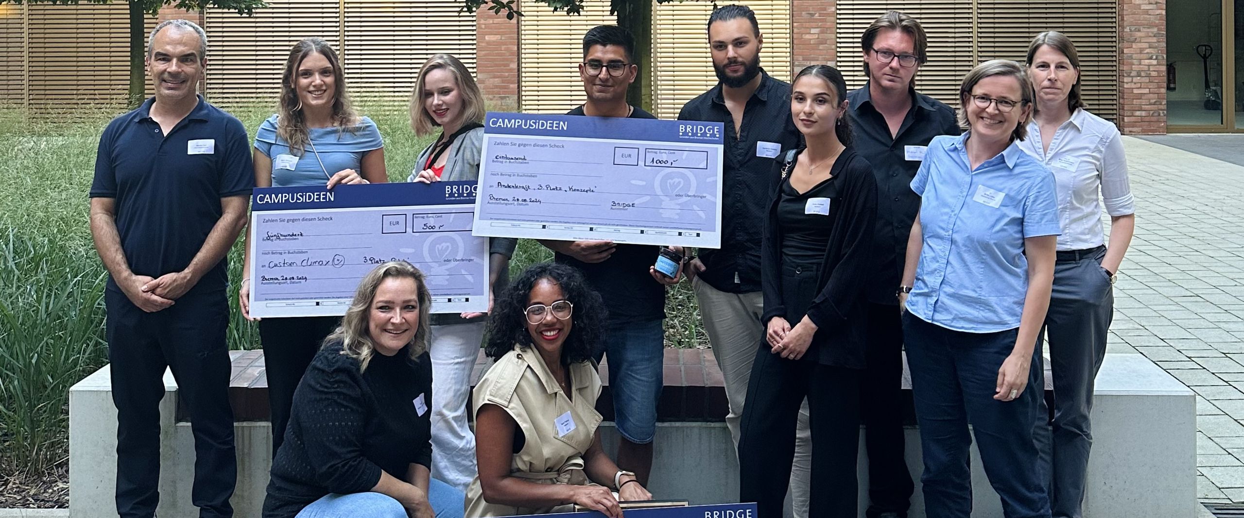 Gruppenbild mit Männern und Frauen. Sie lachen und halten große Checks hoch.