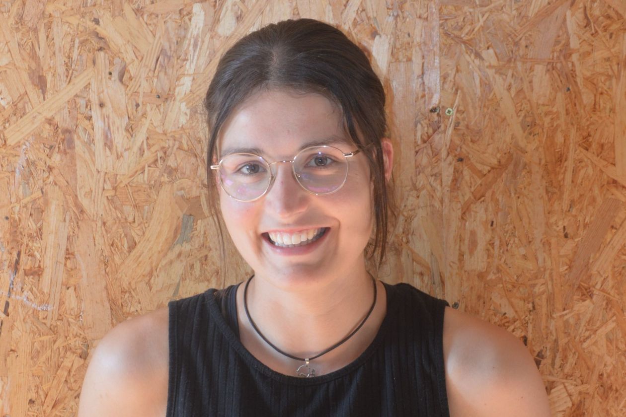 Porträt einer jungen Frau mit Brille und langen braunen Haaren, die zum Zopf gebunden sind.