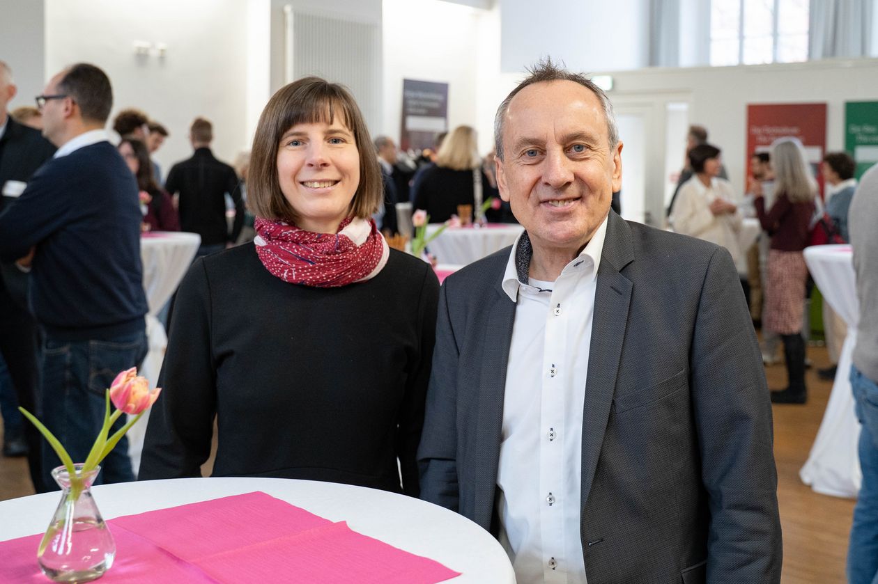 Frau und Mann stehen an einem Tisch und lachen in die Kamera