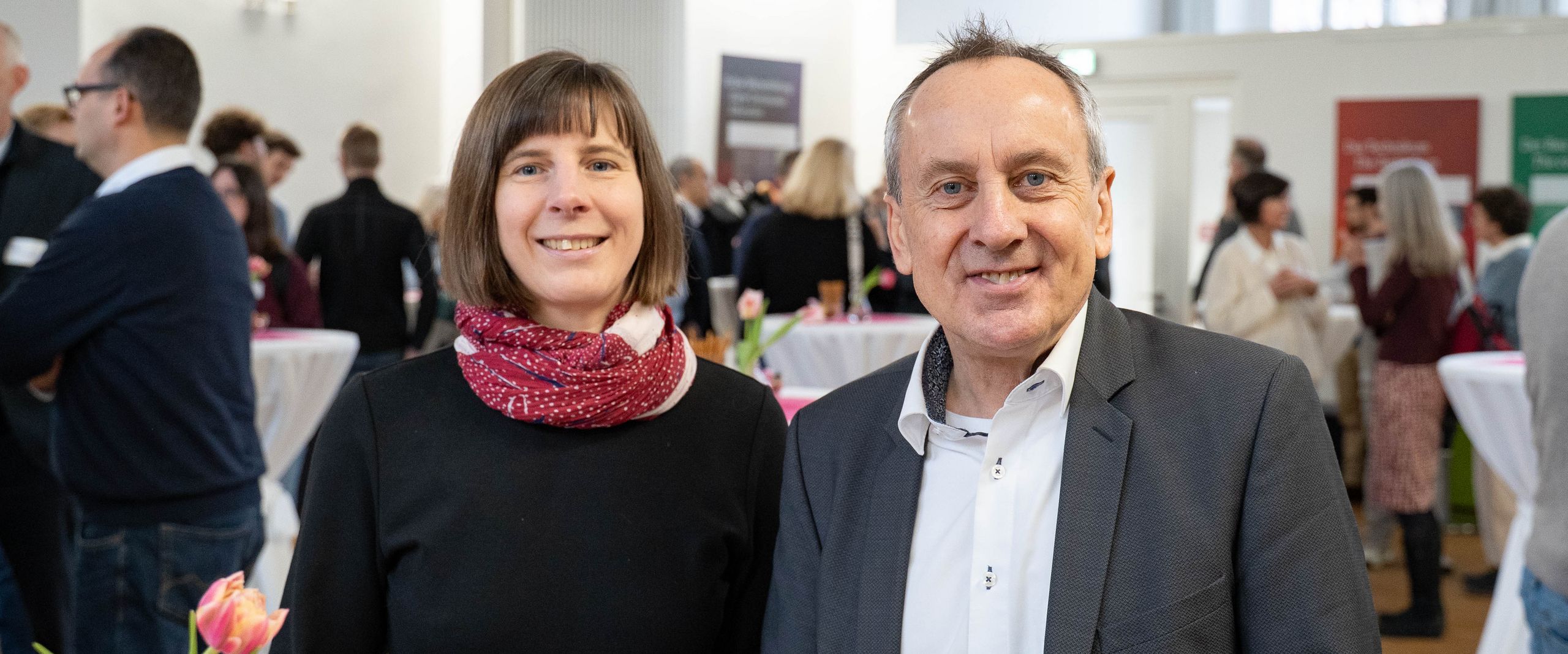 Frau und Mann stehen an einem Tisch und lachen in die Kamera