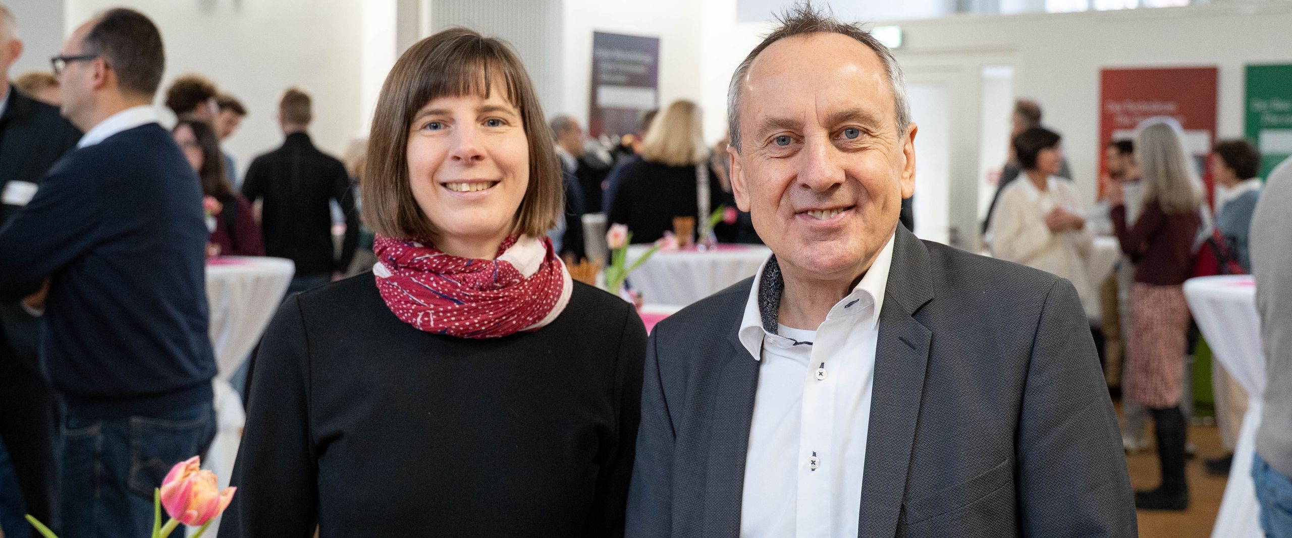 A woman and a man are standing at a table and laughing at the camera.