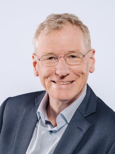 Auf dem Bild ist Hanno Feidicker zusehen. Er hat kurzes graues Haar und trägt eine Brille sowie ein hellblaues Hemd unter einem dunkelblauen Sakko. 