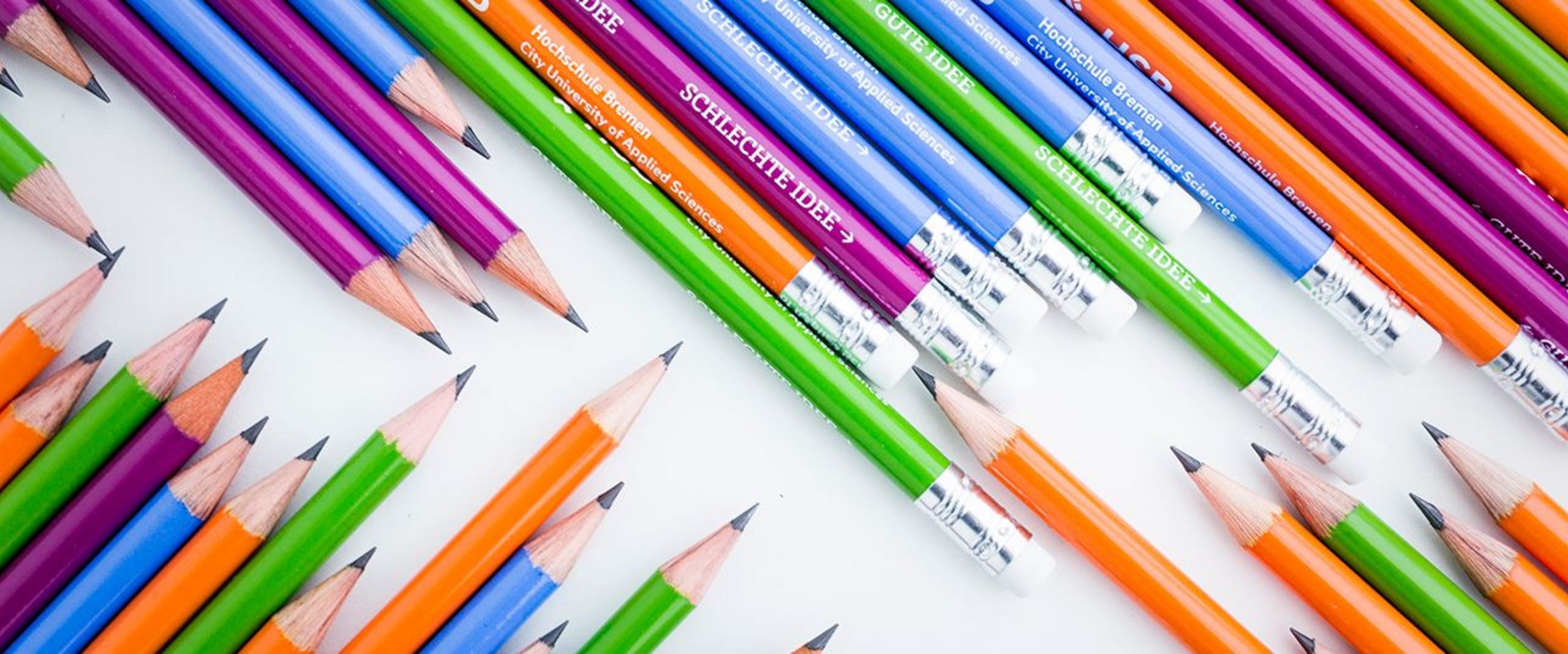 Nebeneinander liegen mehrere blaue, grüne, violette und orangene Bleistifte, die das HSB-Logo tragen.