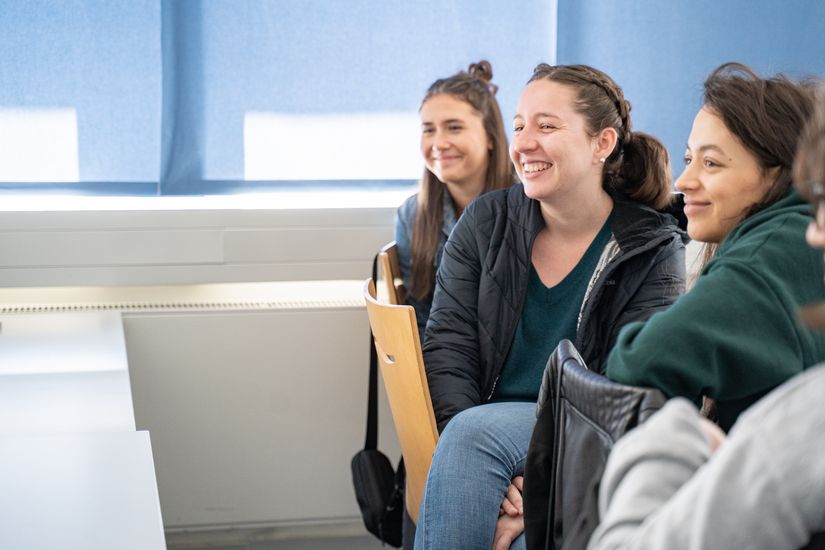 4 junge Studentinnen sitzen an einem langen Tisch und schauen nach links
